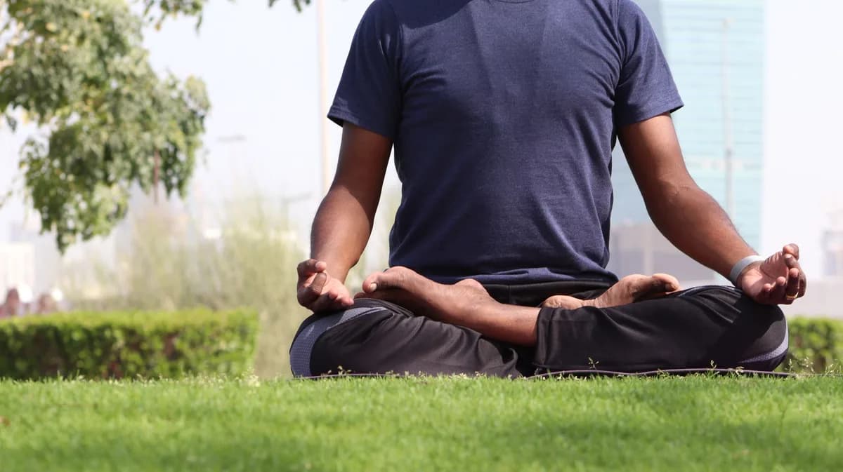 A man practicing meditation in lotus pose on a sunny day in an outdoor urban park.