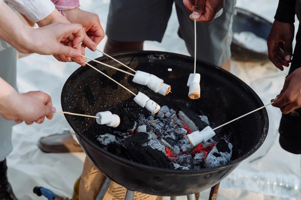 A group of people roasting marshmallows over a charcoal grill at the beach. Perfect summer activity.
