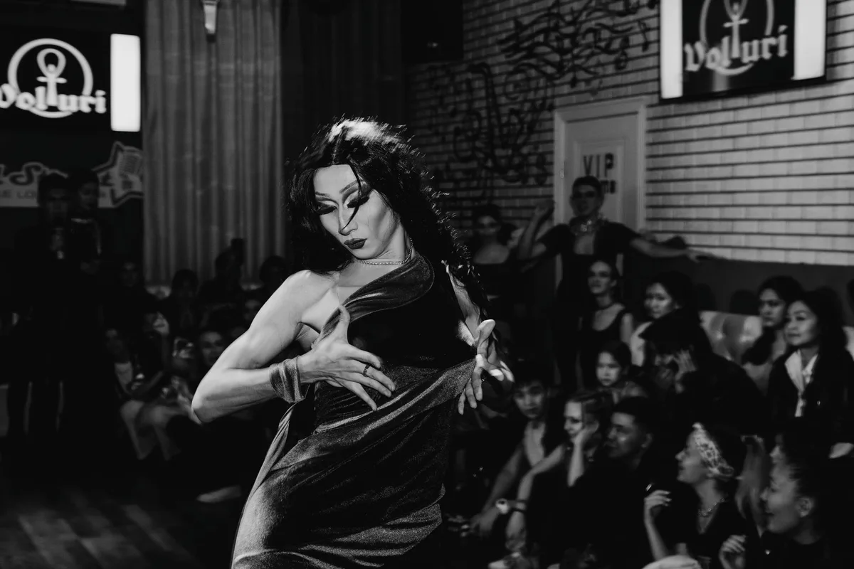 Captivating black and white photo of a drag queen performing for an audience in a nightclub.