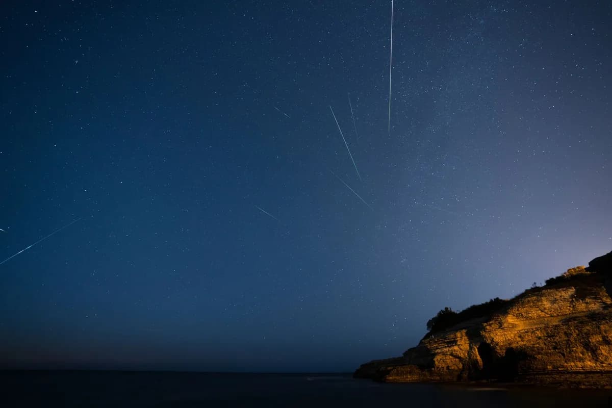 Meteors streaking across a starry sky above a rocky landscape.