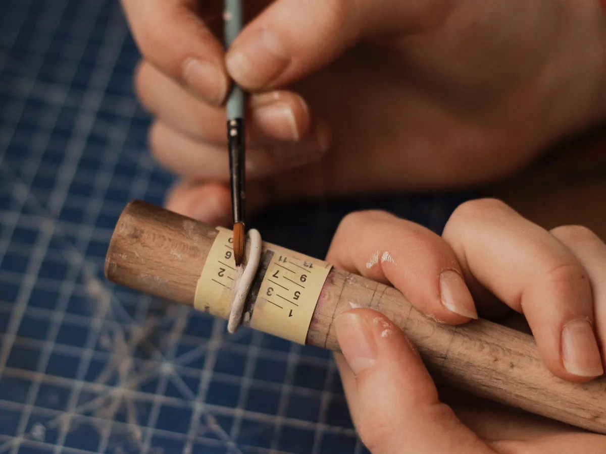 An artisan carefully paints a handmade ring using a brush at their workspace.