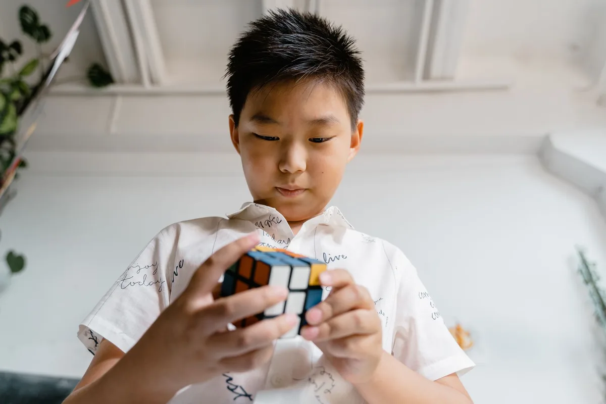 Young boy intently solving a Rubik's Cube, displaying concentration and skill indoors.