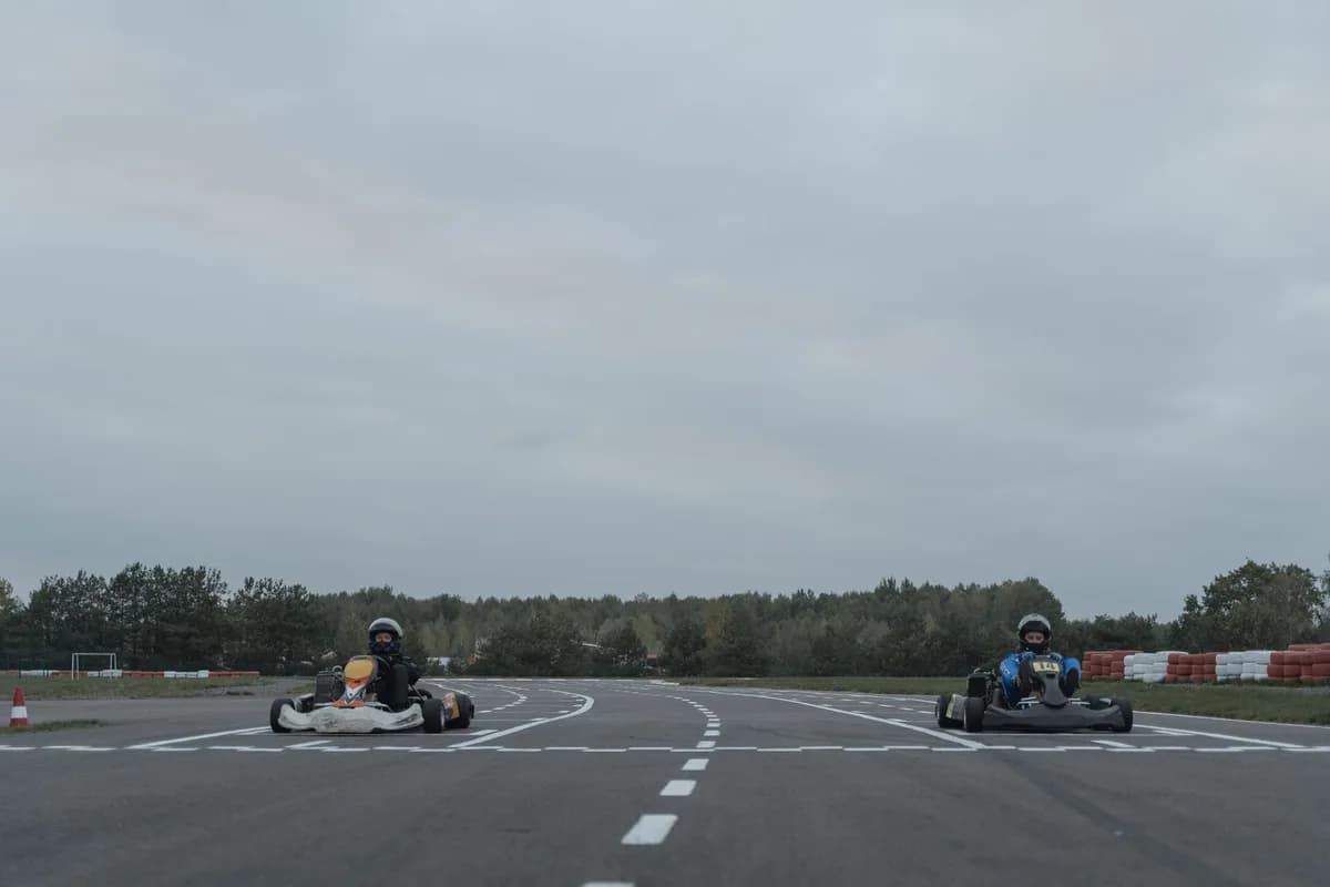 Two athletes racing go-karts on an outdoor racetrack in overcast conditions.