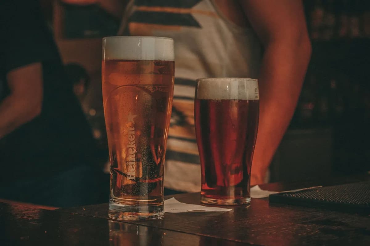 Close-up of two pints of beer on a bar counter in a lively pub setting.