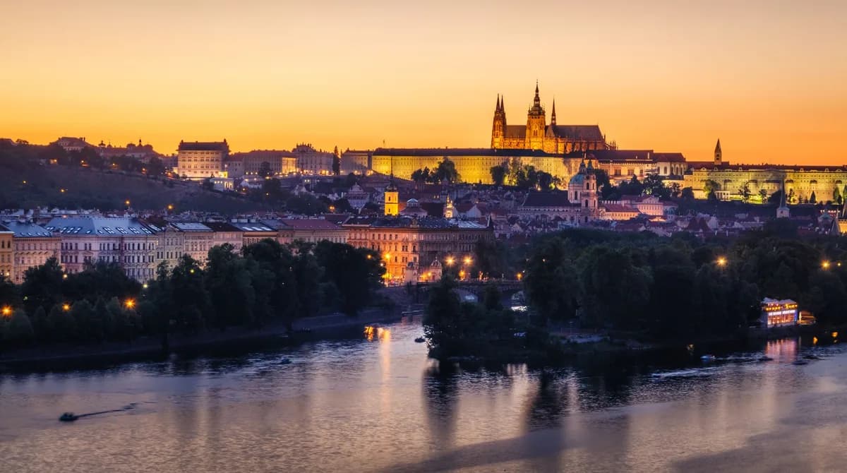 Scenic view of Prague Castle glowing at sunset with the Vltava River in the foreground.