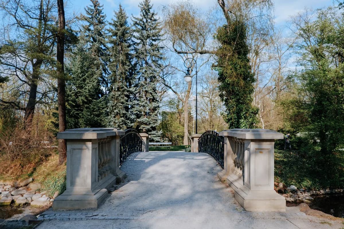 Elegant stone bridge surrounded by lush greenery in a serene park atmosphere.