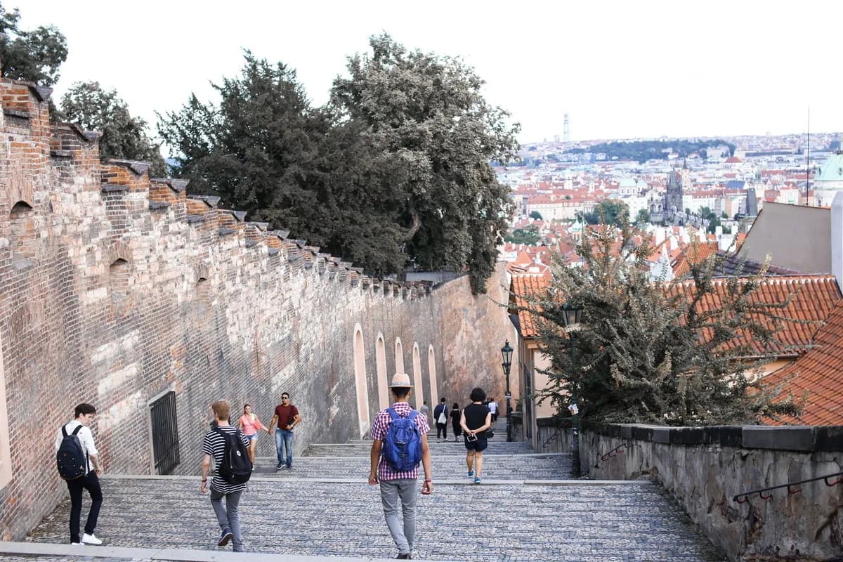 Tourists walking along the historic walls of Prague Castle with panoramic city views.