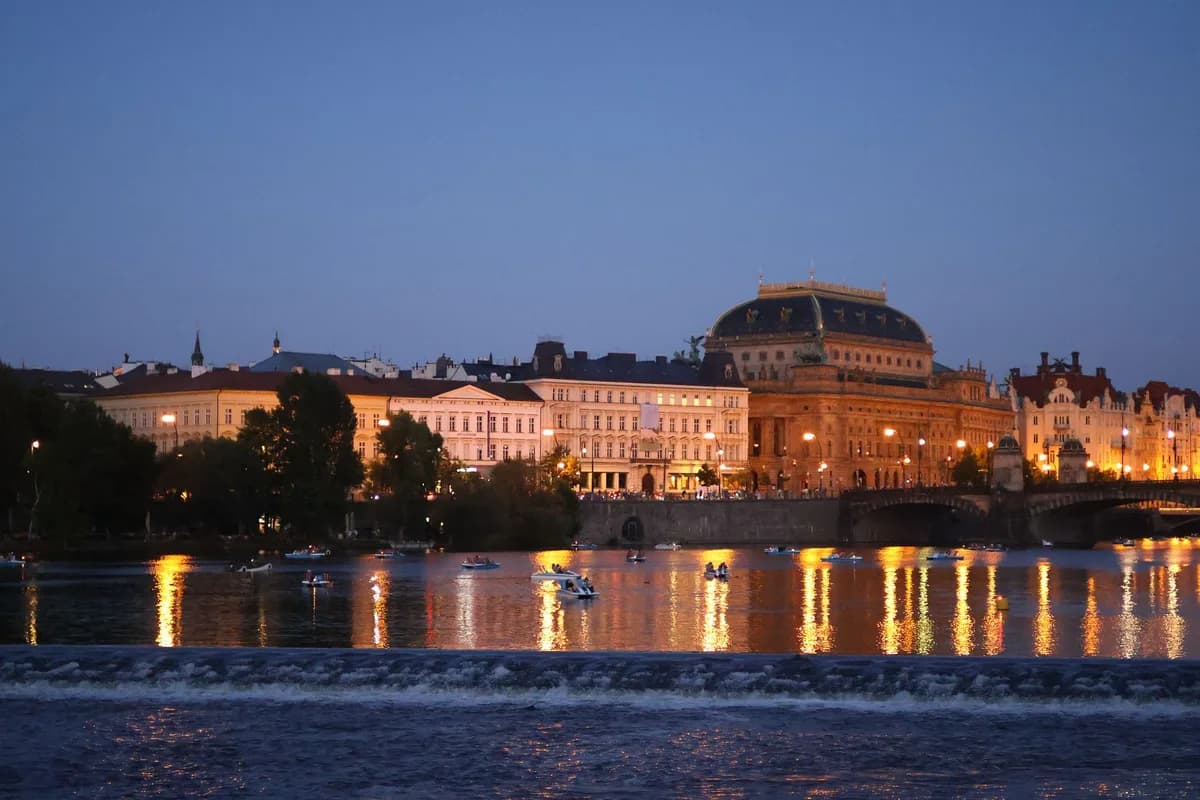 View of Prague's National Theatre and Vltava River illuminated at dusk.