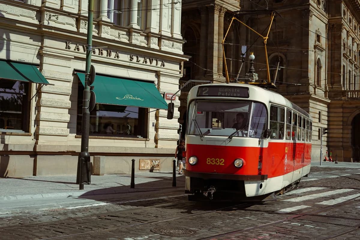 Red tram passes by historic buildings in Prague's city center on a sunny day.