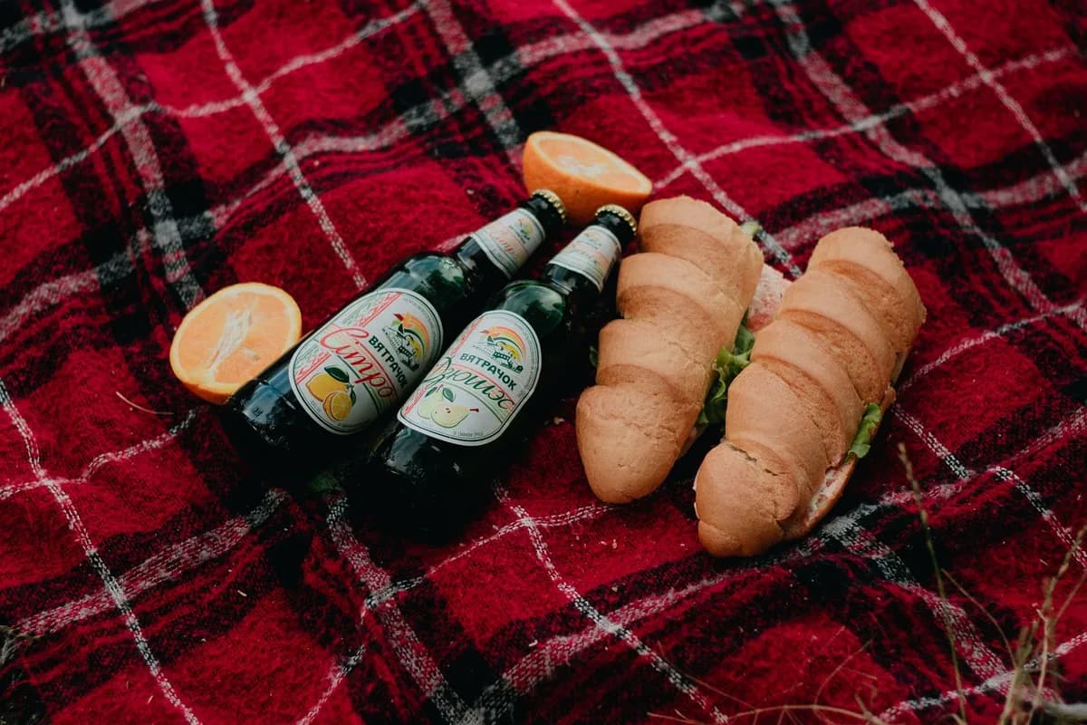 Enjoy a cozy picnic with beer, baguettes, and fresh oranges on a red plaid blanket.