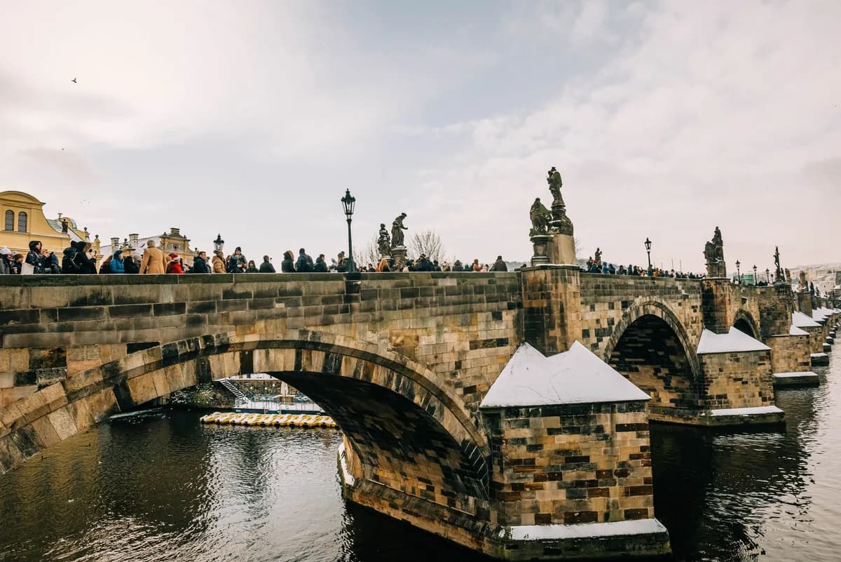 Tourists walking along Charles Bridge in Prague on a crisp winter day, showcasing its Gothic architecture.