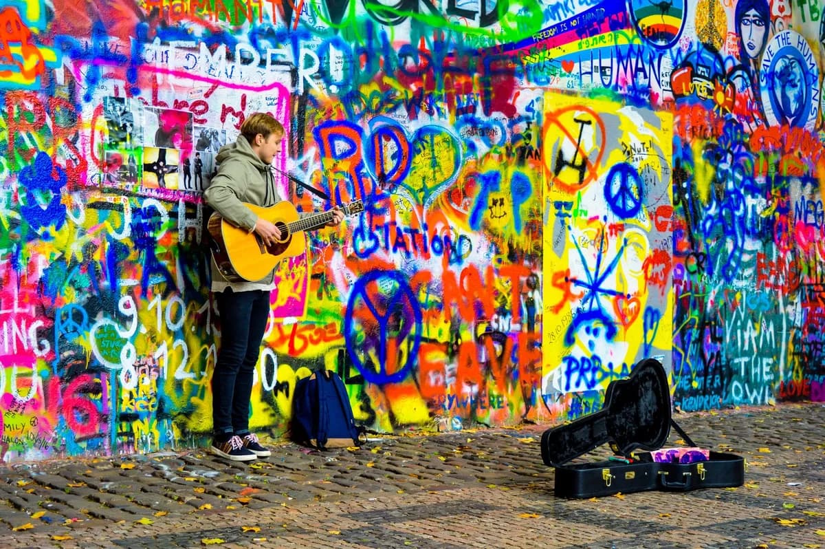 Street musician plays guitar in front of a colorful graffiti wall. Artistic urban scene.