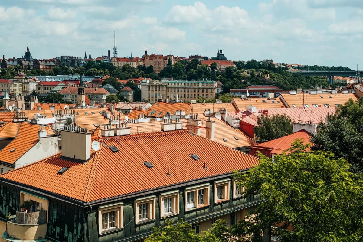 Panoramic view of red-tiled rooftops and historic architecture under a blue sky in Europe.