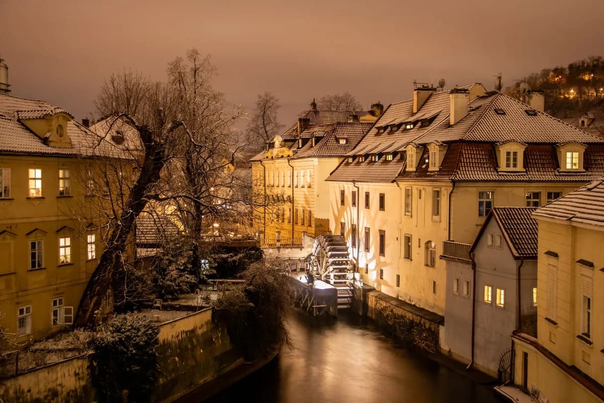 Charming snow-covered architecture and water mill at night in historic Prague.