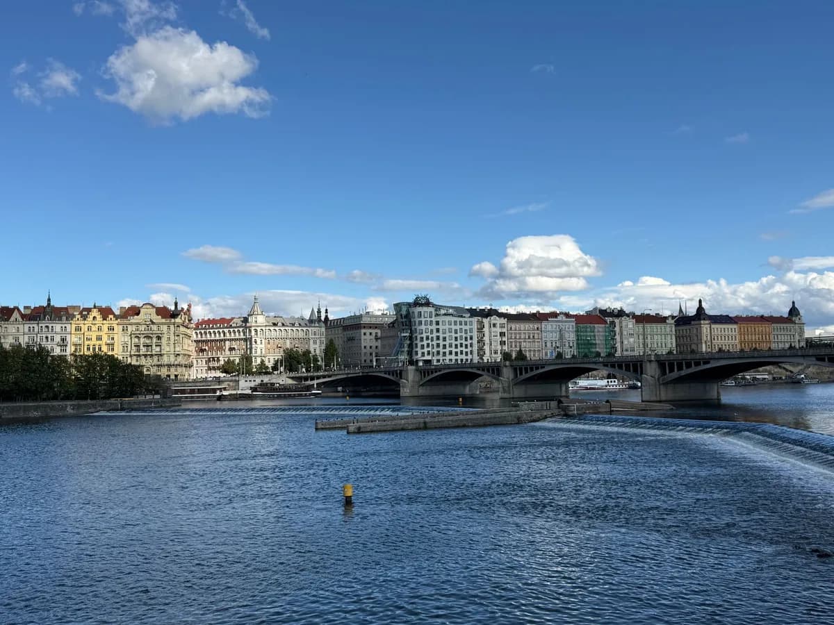 Picturesque view of the Vltava River in Prague with historical buildings and bridge. Clear sky enhances the city's charm.