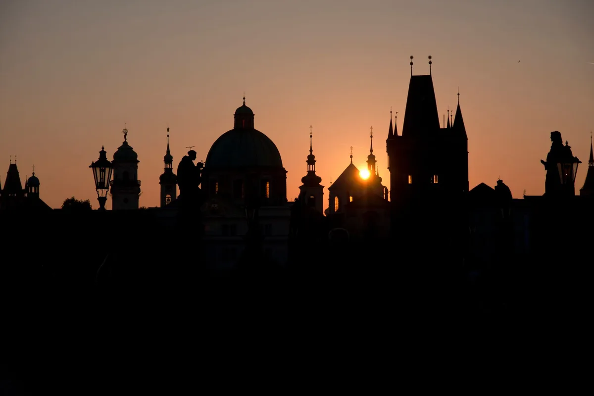 Silhouette of Prague's historic skyline against a vibrant sunset backdrop.